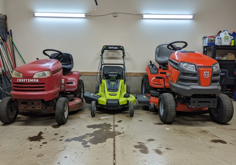 Three different brand lawn mowers stored in residential garage showing Craftsman, Ryobi and Husqvarna models