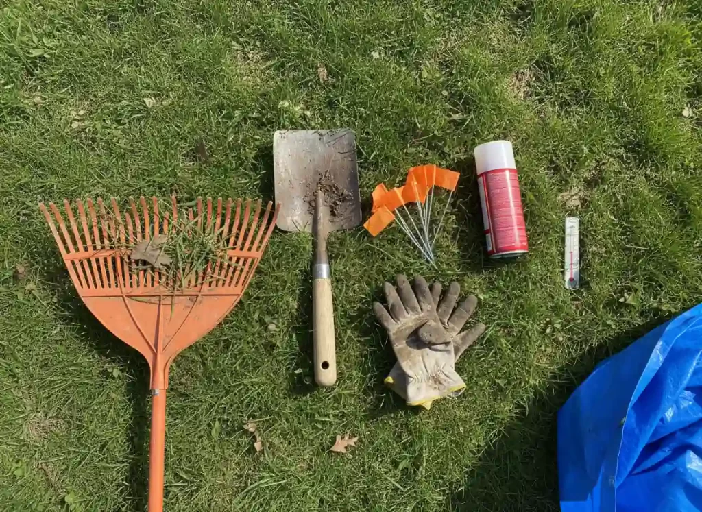 Spring lawn care cleanup tools including leaf rake flat spade soil thermometer and marking flags on grass